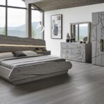 Best Grey Oak Bedroom Furniture Guide Modern grey bedroom with a sculptural wood bed, integrated LED headboard and floating nightstands, matching dresser with mirror and large wardrobe featuring abstract groove patterns, set in a high-ceiling room with floor-to-ceiling windows overlooking forested hills.